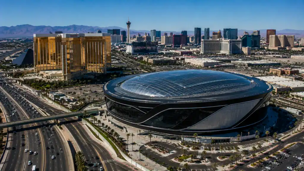 Aerial daytime view of Allegiant Stadium in Las Vegas with the dome gleaming in Nevada sunshine and Mandalay Bay hotel and the Las Vegas Strip visible in the background