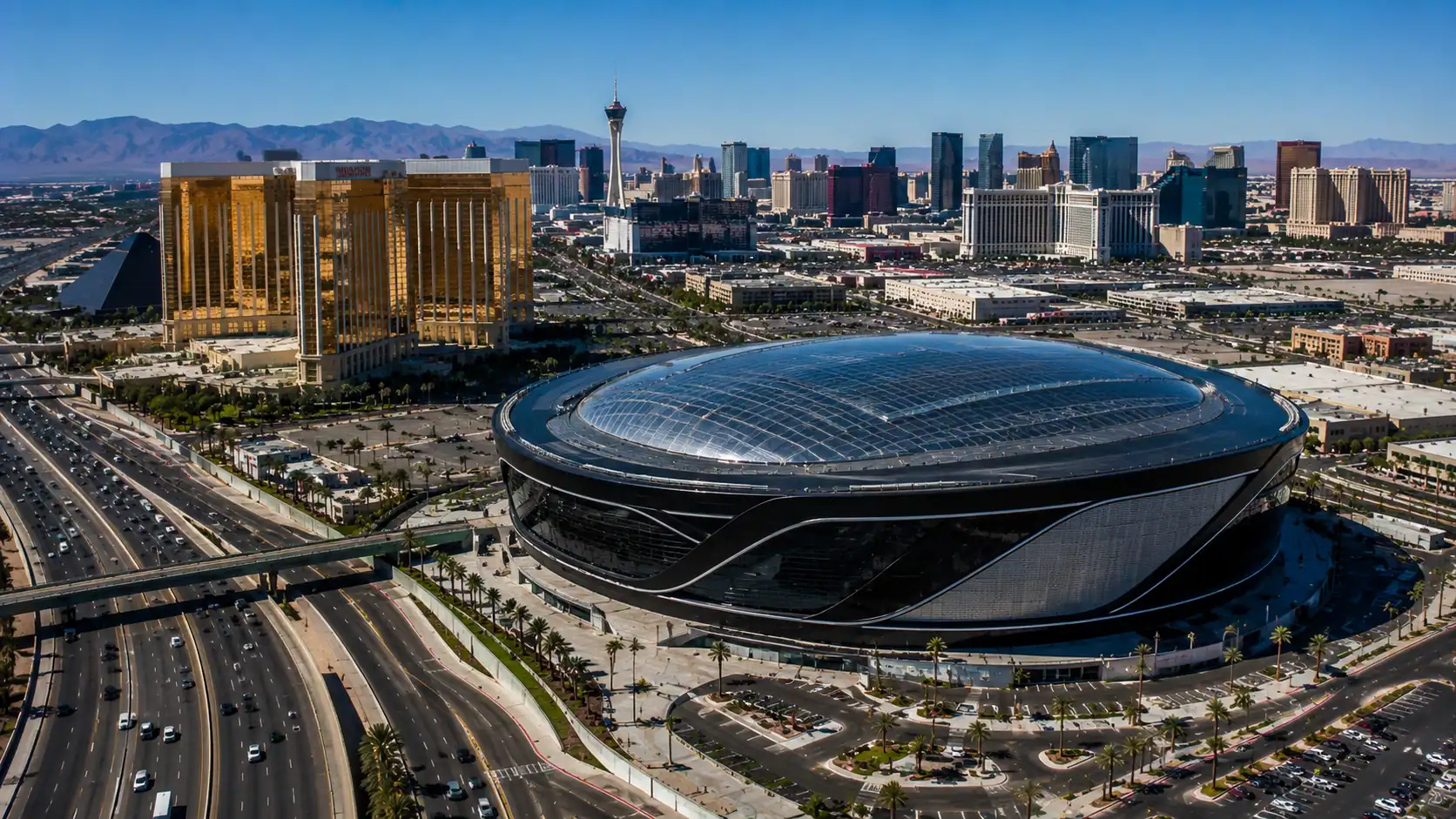 Aerial daytime view of Allegiant Stadium in Las Vegas with the dome gleaming in Nevada sunshine and Mandalay Bay hotel and the Las Vegas Strip visible in the background
