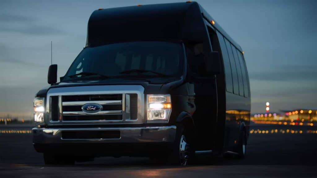 Black E450 Shuttle Bus At Dawn With Headlights