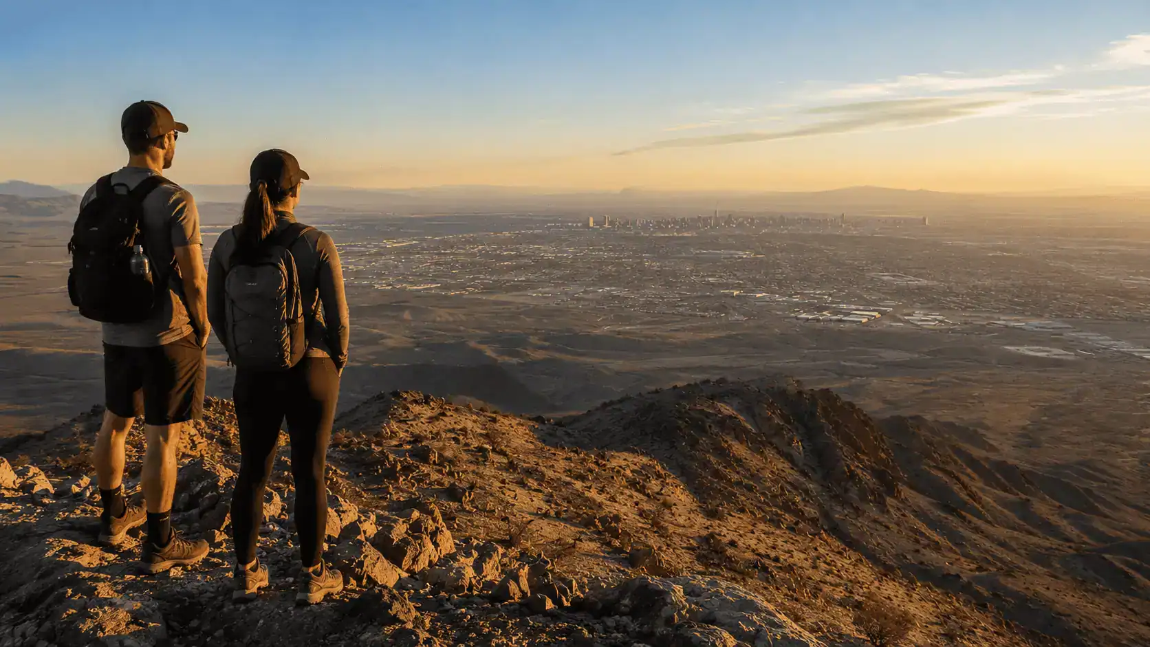 Frenchman Mountain Summit Hikers Overlooking Las Vegas Valley Golden Hour – Personal Sedan Services Hikers at the summit of Frenchman Mountain in Sunrise Manor Nevada looking out over the Las Vegas Valley with the Strip in the distance at golden hour