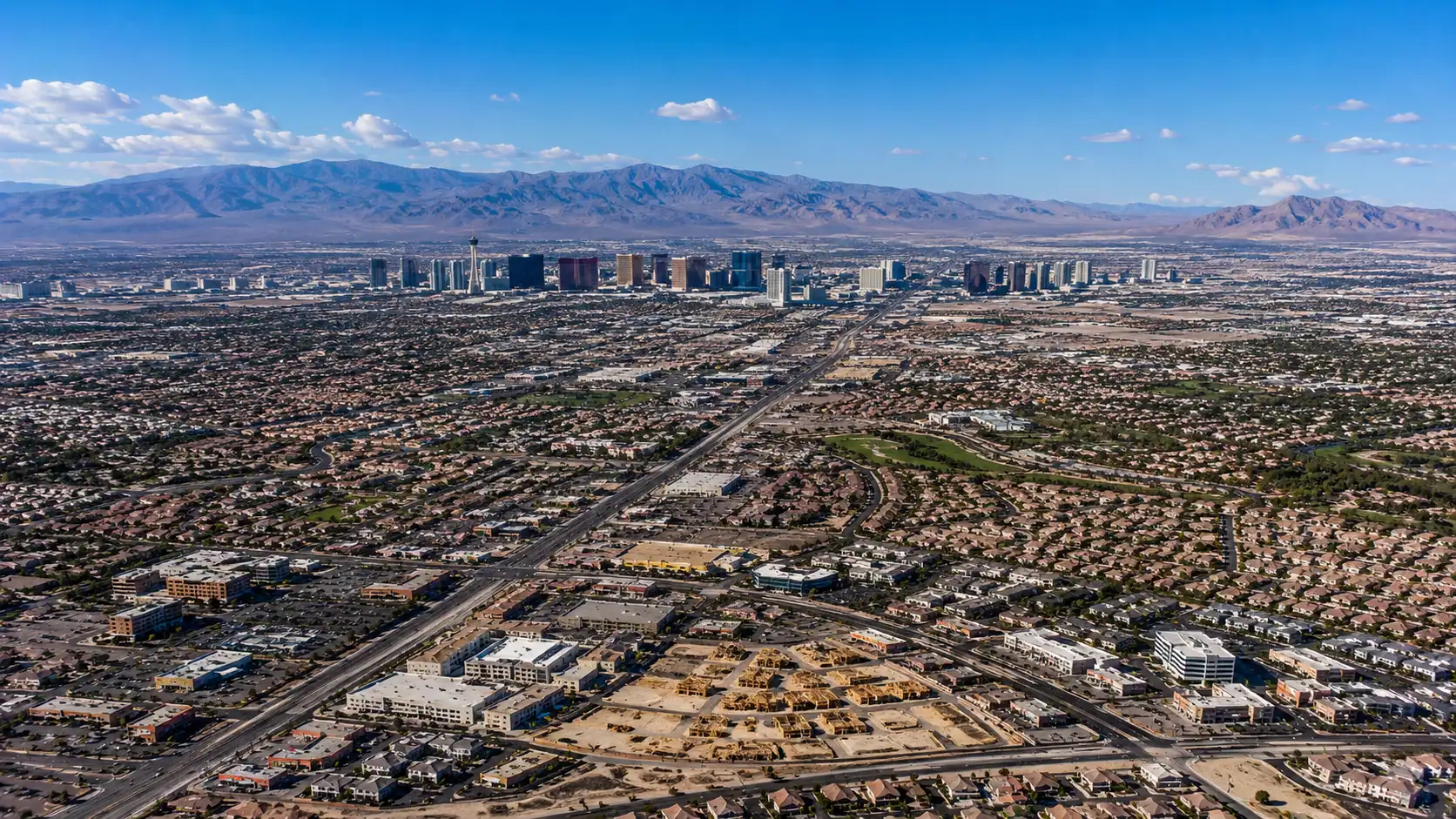 Aerial daytime view of the Las Vegas Valley showing residential suburbs in all directions from the Strip corridor toward mountain ranges representing the population and real estate statistics of the Las Vegas metropolitan area