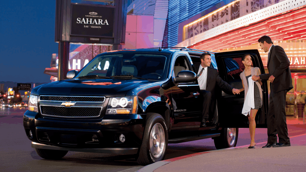 Newer Black Chevrolet Suburban Suv With Driver Chauffeur Wearing A Suit And Passengers Leaving From The Back Seat Dropping Them Off In Las Vegas At The Sahara
