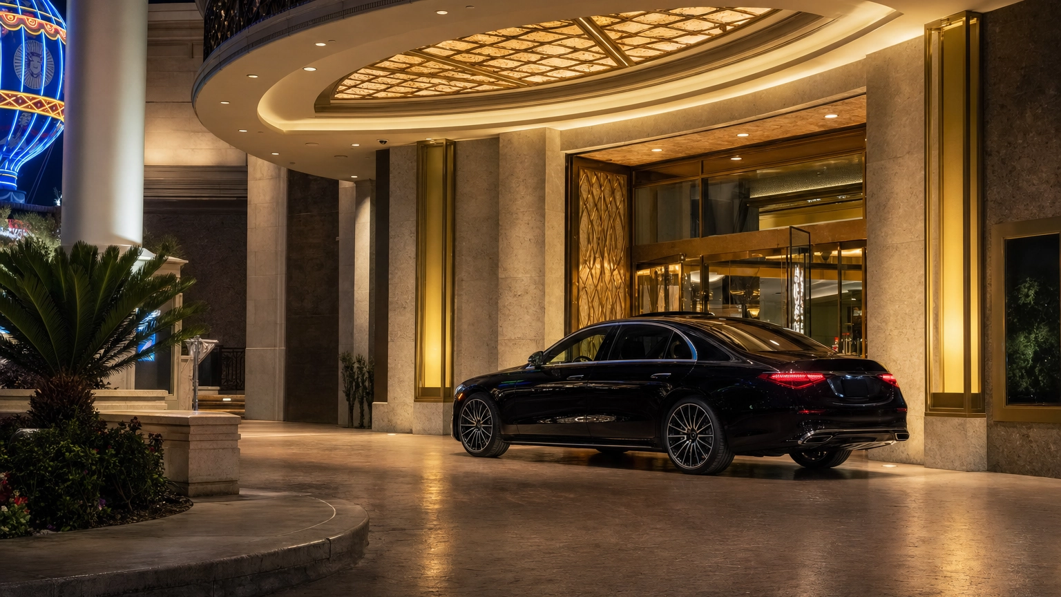 Glossy black luxury sedan waiting at a brightly lit Las Vegas theater entrance at night
