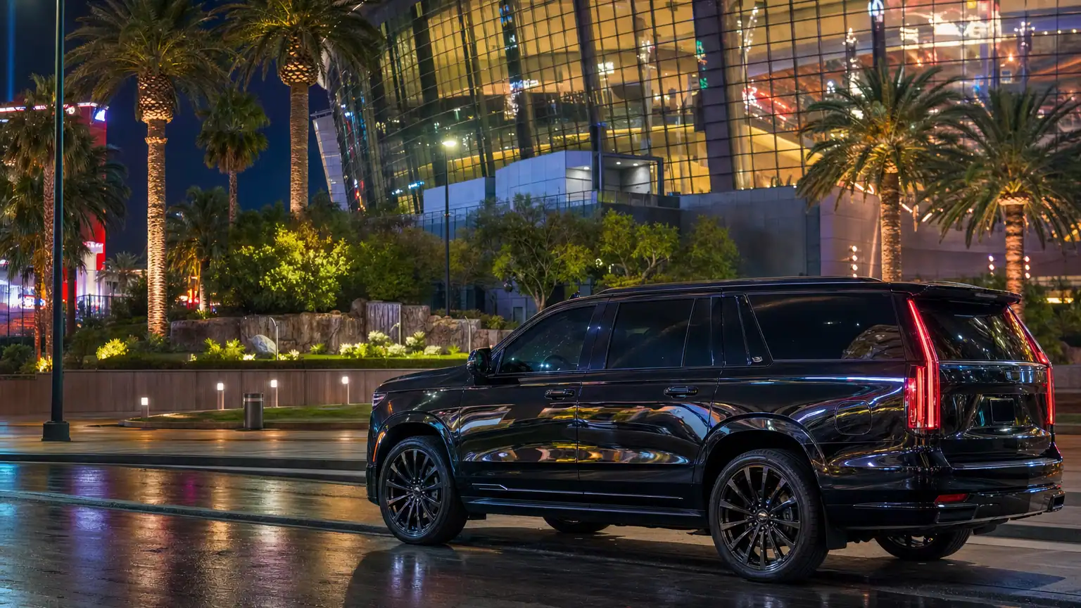 Glossy black luxury SUV parked outside a modern Las Vegas Strip arena at night with neon glow on wet pavement