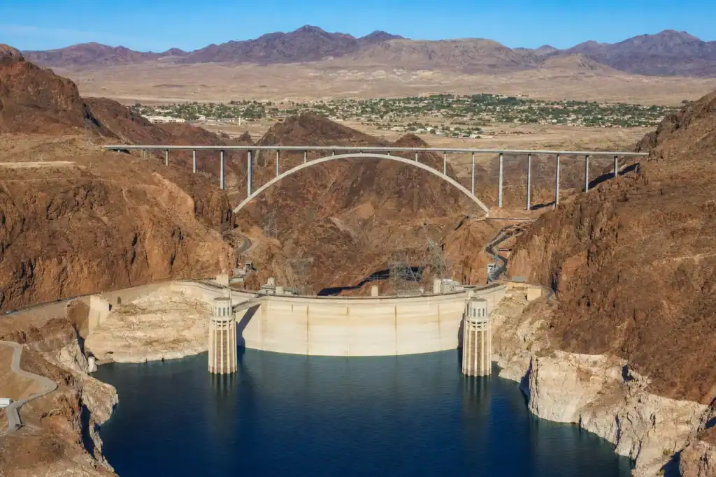 Hoover Dam holding back Lake Mead with the memorial bridge above and the historic town of Boulder City Nevada on the plateau beyond