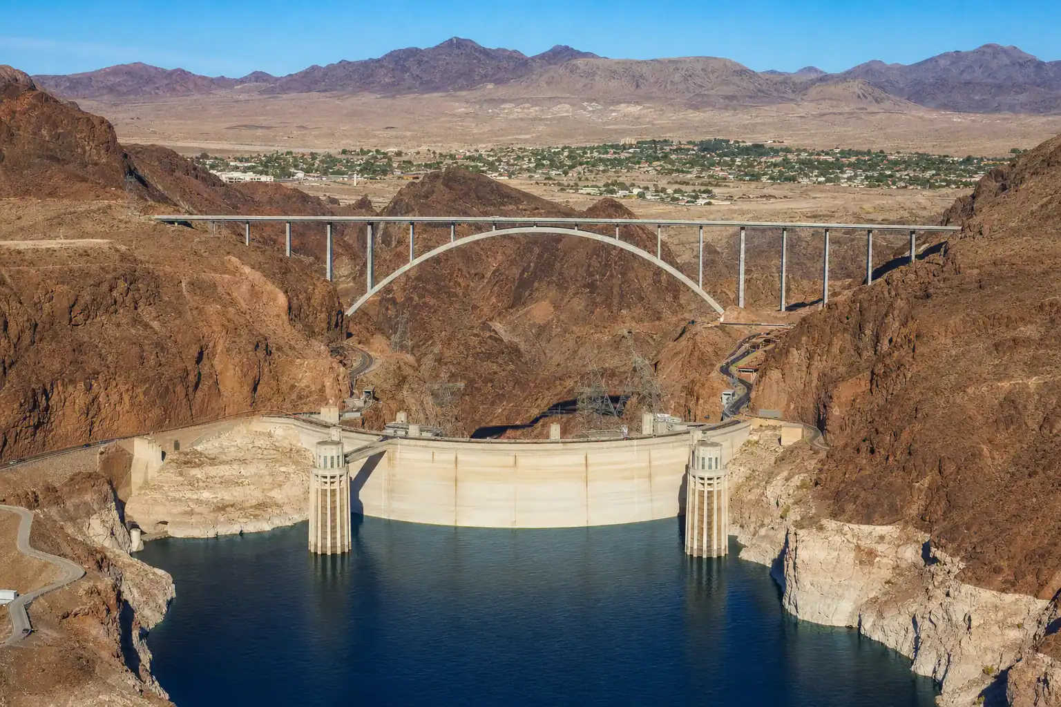 Hoover Dam holding back Lake Mead with the memorial bridge above and the historic town of Boulder City Nevada on the plateau beyond