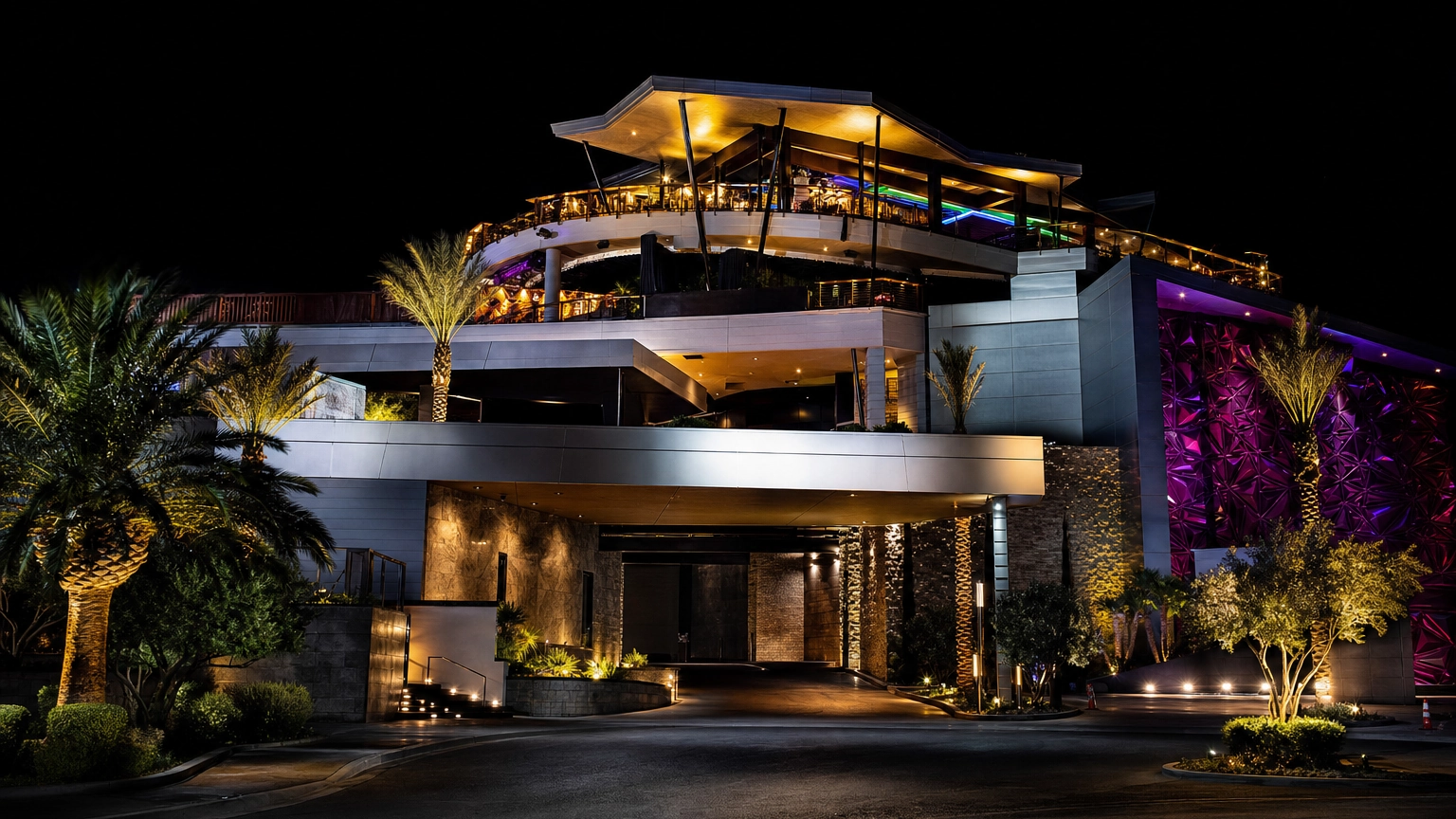 Tall multi-level Las Vegas gentlemen's club exterior with a glowing rooftop deck at night, in the style of Larry Flynt's Hustler Club