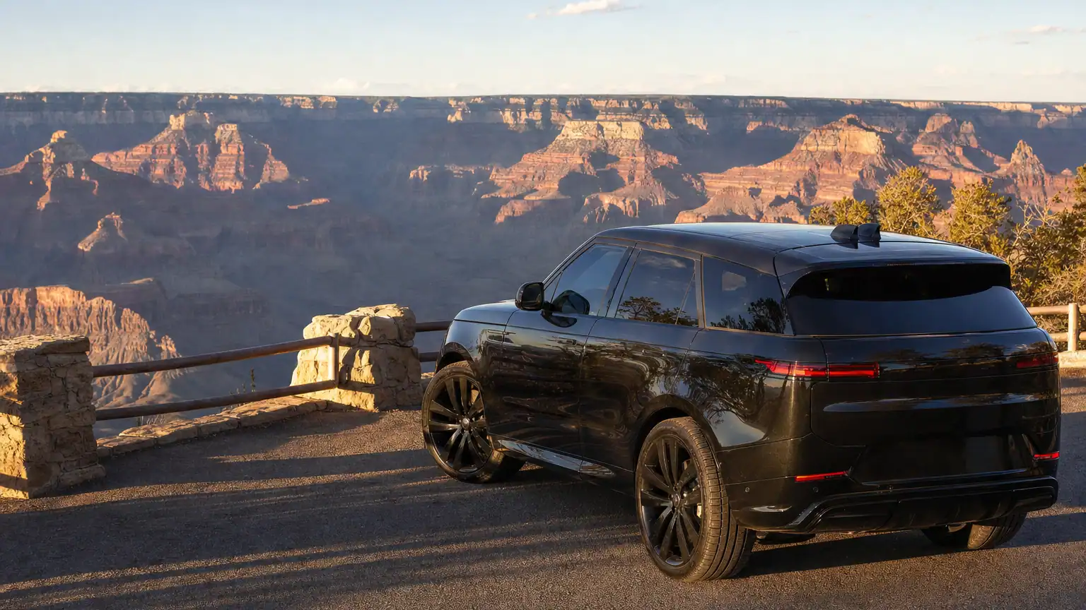 Black luxury SUV parked at a Grand Canyon rim overlook at golden hour with layered canyon walls behind