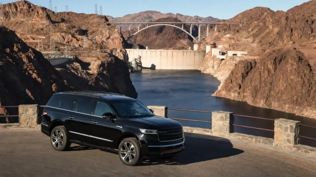 Black luxury SUV parked at an overlook above Hoover Dam, the Colorado River and Memorial Bridge at golden hour