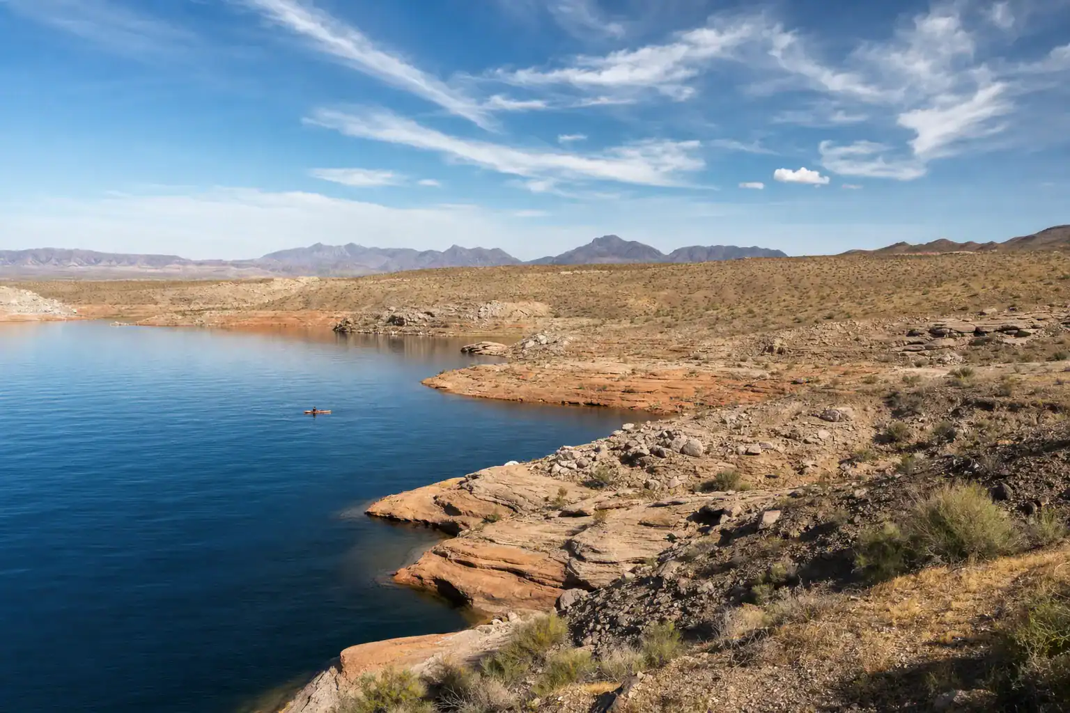 Overton Arm Lake Mead Cove Kayak Moapa Valley Nevada Desert Shoreline – Personal Sedan Services A calm cove on the Overton Arm of Lake Mead near Moapa Valley Nevada with blue water, red desert shoreline, and a kayak